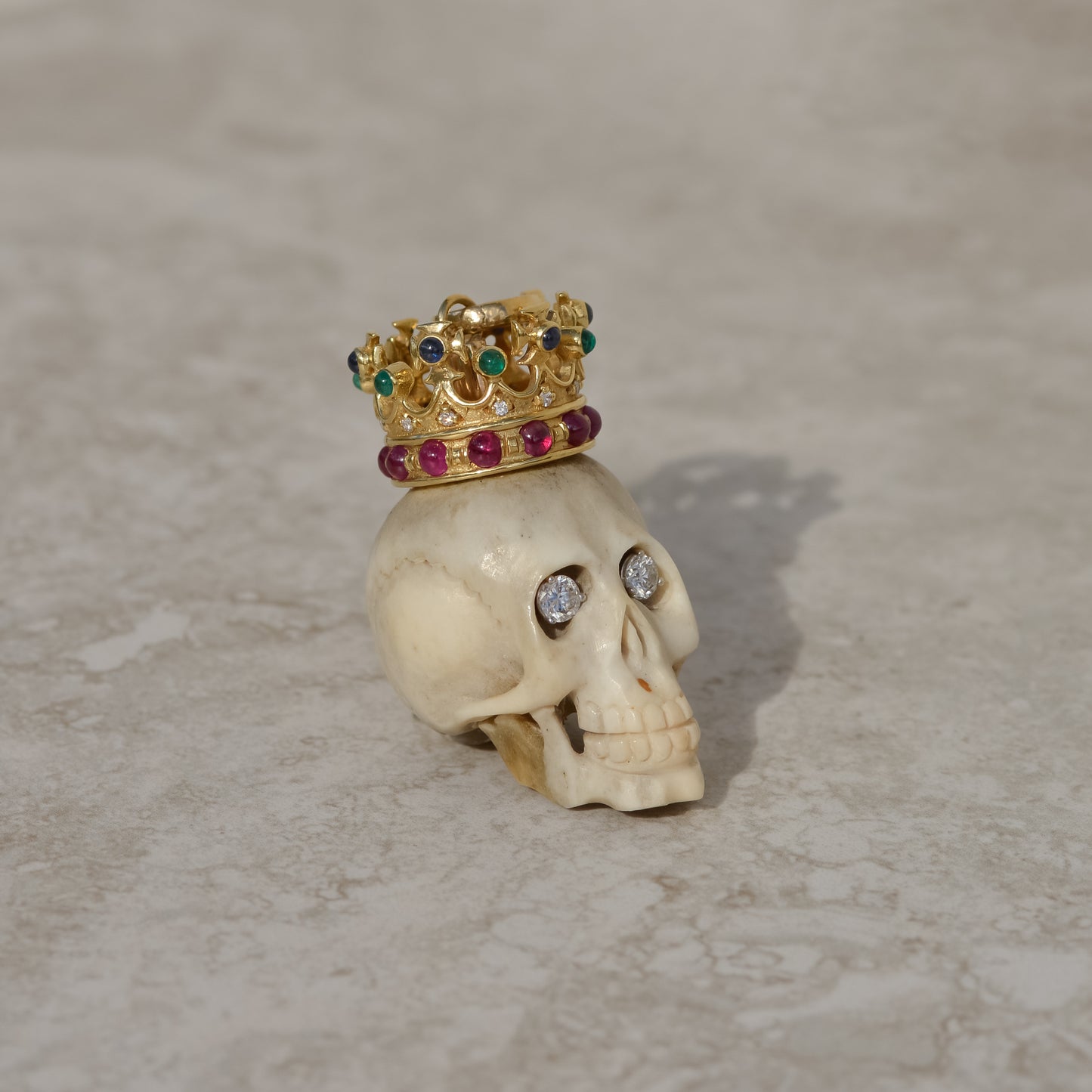 Carved bone skull pendant with diamond eyes and 14k gold crown set with diamonds, rubies, emeralds, and sapphires.