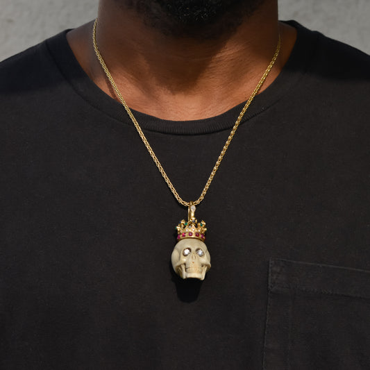 Carved bone skull pendant with diamond eyes and 14k gold crown set with diamonds, rubies, emeralds, and sapphires, worn on a gold wheat chain.