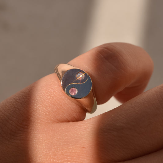 Gold ring with a yin yang design on a person's finger against a neutral background