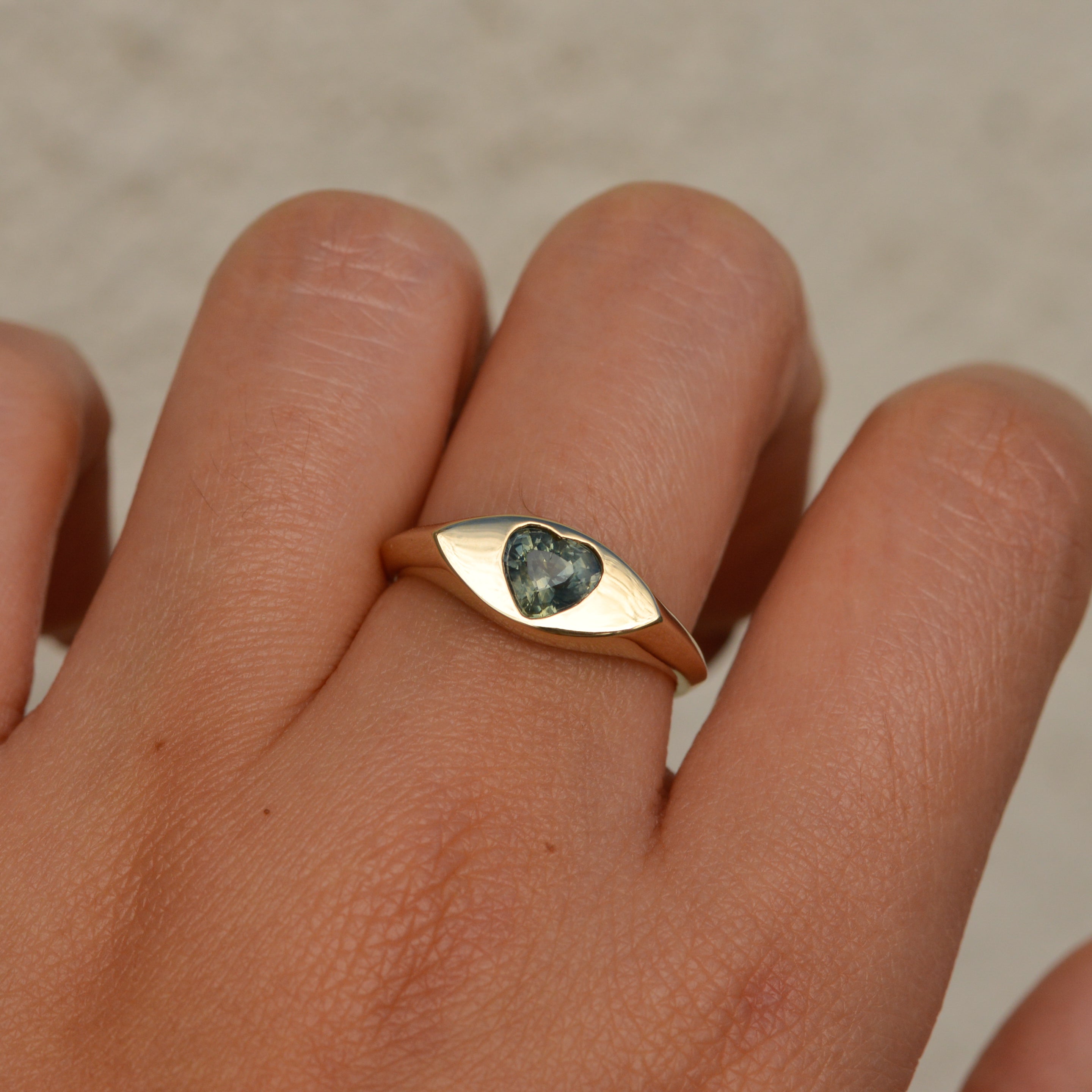 14k gold eye-shaped signet ring, with a flush set heart cut parti sapphire displaying blue and yellow colors