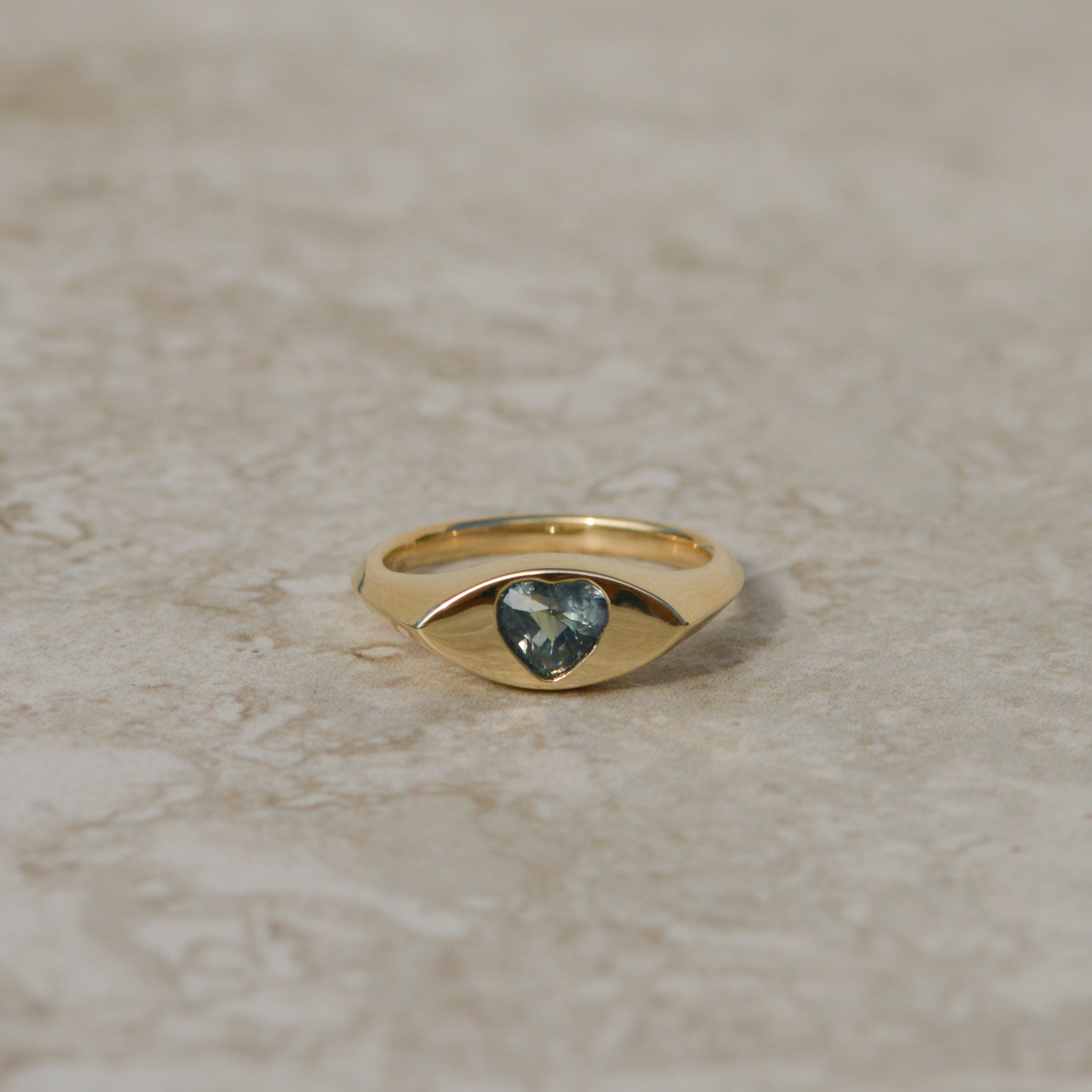 14k gold eye-shaped signet ring, with a flush set heart cut parti sapphire displaying blue and yellow colors