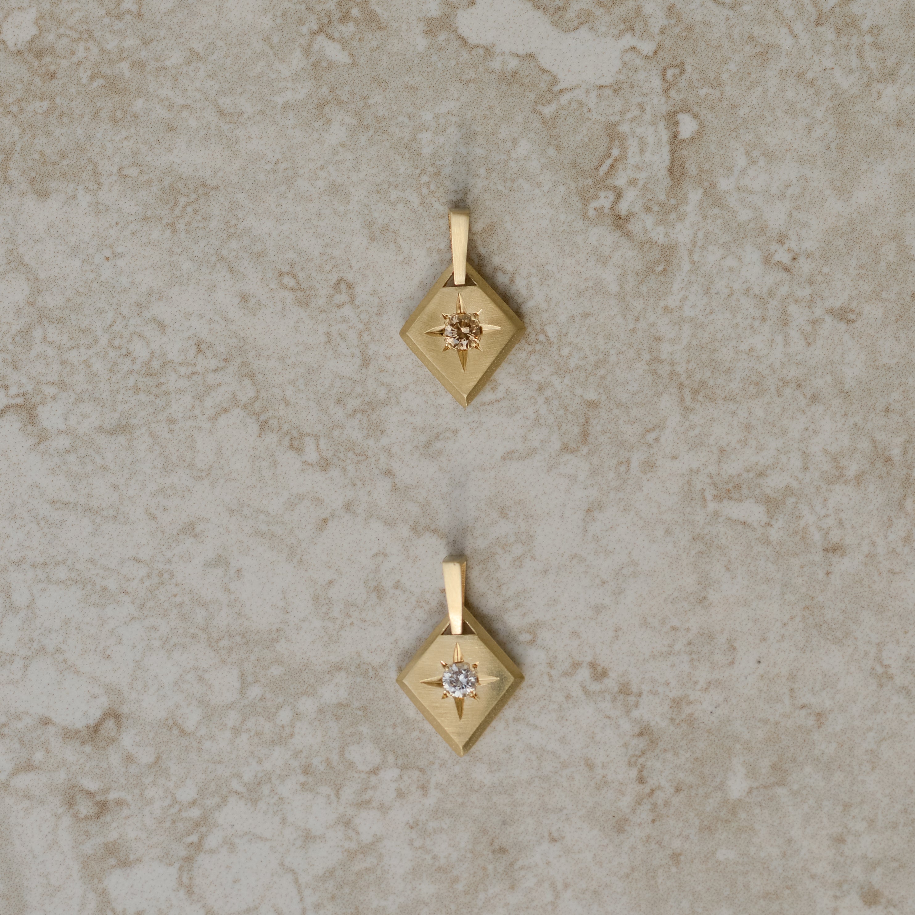 Two lozenge-shaped tag pendants with star set round brilliant cut diamonds, one champagne color, one white