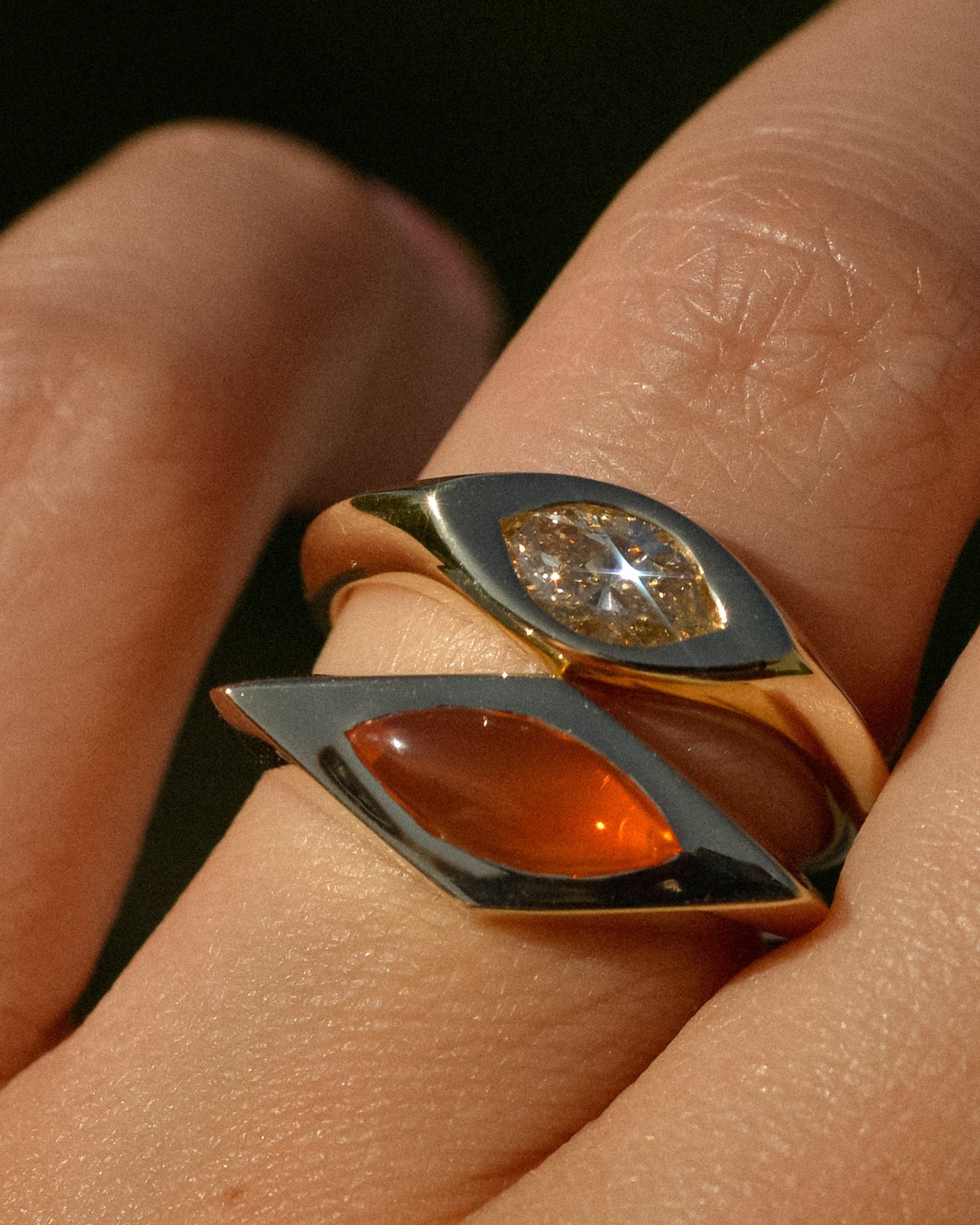 Close-up of a hand wearing two gold rings with gemstones on a dark background