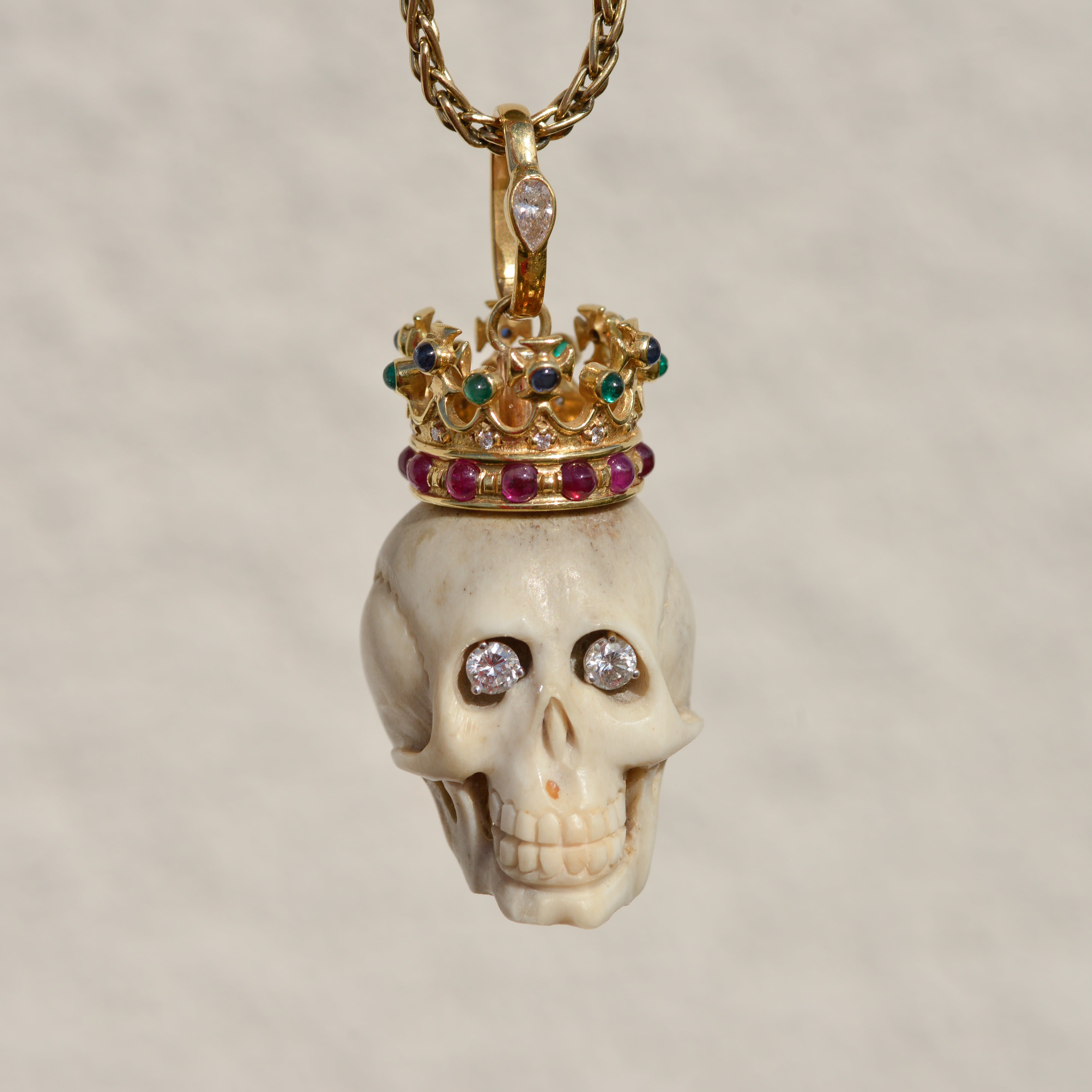 Carved bone skull pendant with diamond eyes and 14k gold crown set with diamonds, rubies, emeralds, and sapphires.