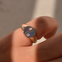 Gold ring with a yin yang design on a person's finger against a neutral background